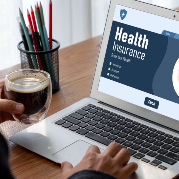 AdobeStock_536319968 Woman sitting at brown desk on laptop viewing Health insurance web site