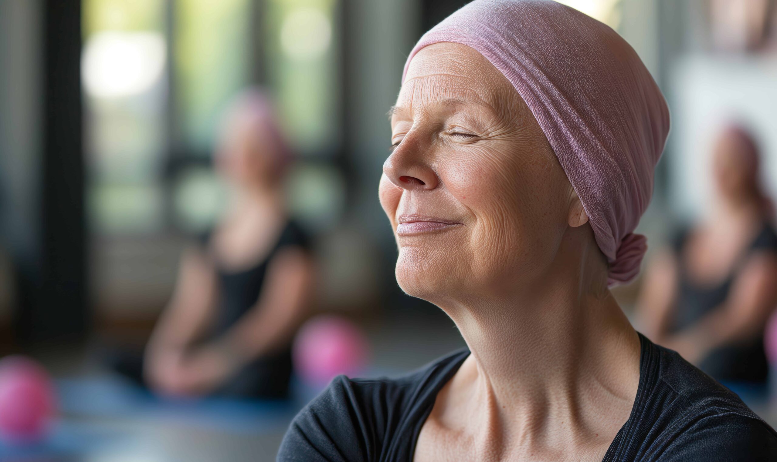 AdobeStock_912419457 close-up portrait of an elderly cancer survivor with a pink headscarf, smiling during a yoga class in the gym